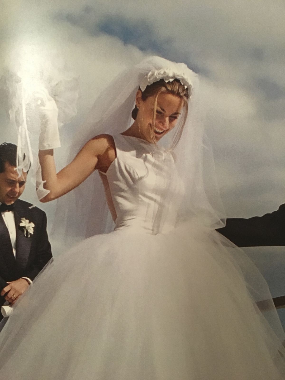 Vintage bride laughing in a full tulle ball gown and veil, being helped down a set of steps